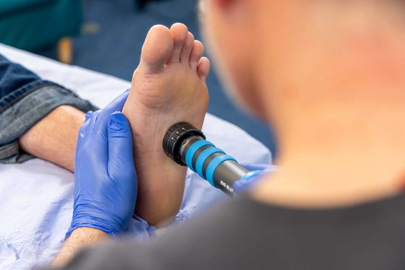 Tall green trees with lush foliage line a pathway under a clear blue sky. A sign indicating a health center is visible on the right side, partially obscured by the trees.